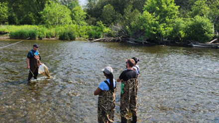 Instructor and three participants stand in a river wearing waders