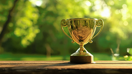 A gleaming golden trophy sits elegantly on a wooden table. surrounded by a lush green garden filled with soft bokeh lights