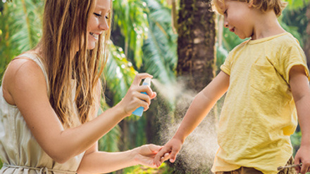 Mom spraying kids arm with sunscreen