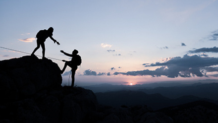 Person reaching hand to help other persoon climb mountain